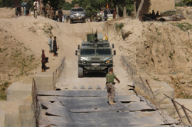 Vehículos militares españoles Vamtac, se disponen a cruzar el único puente viable de la zona.