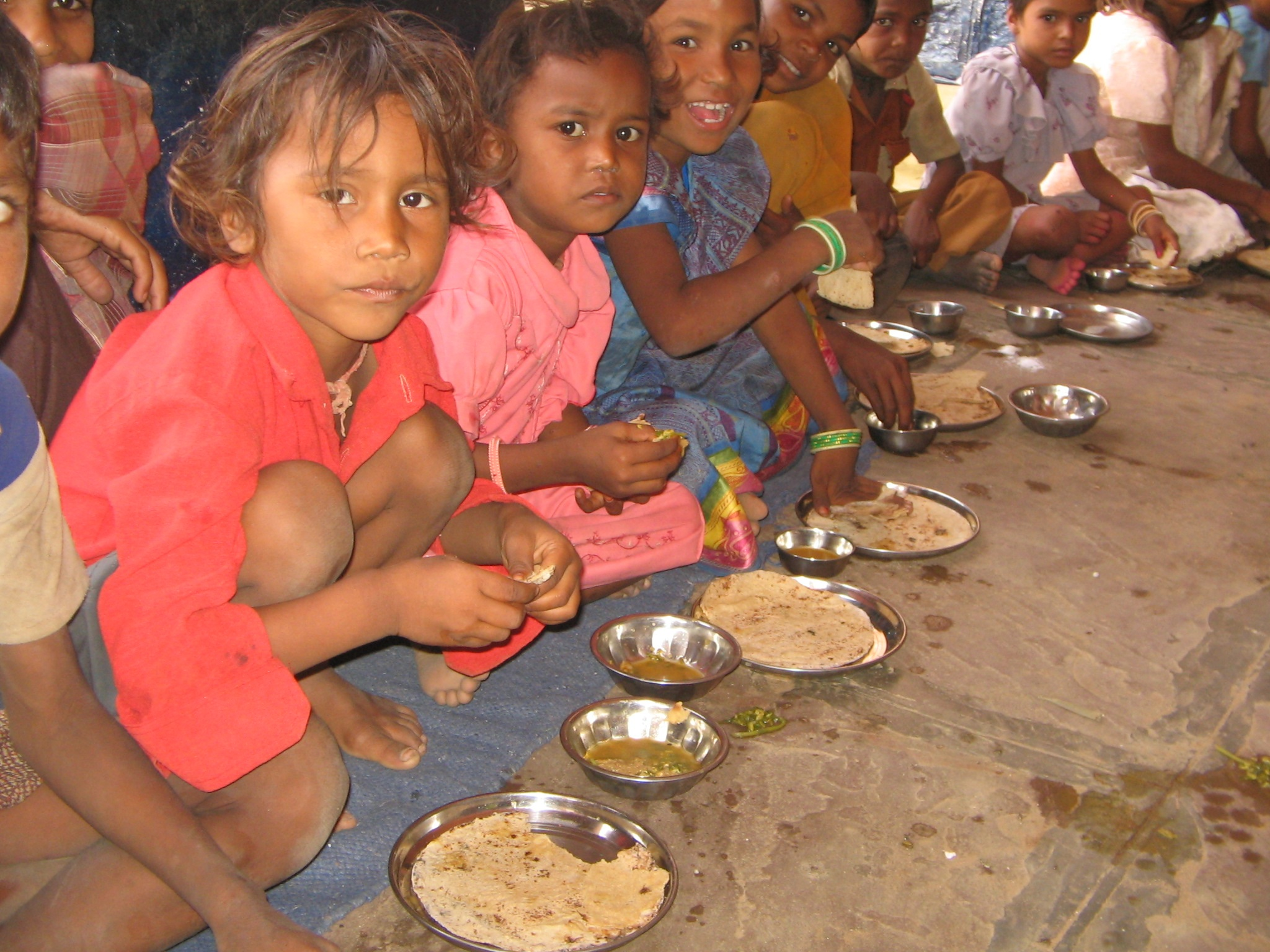 Niños en el suelo comiendo de un plato metálico
