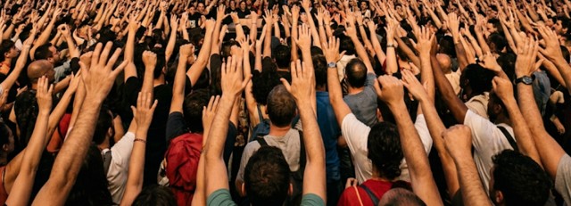 Una multitud de personas de espaldas levantando los brazos en un evento masivo